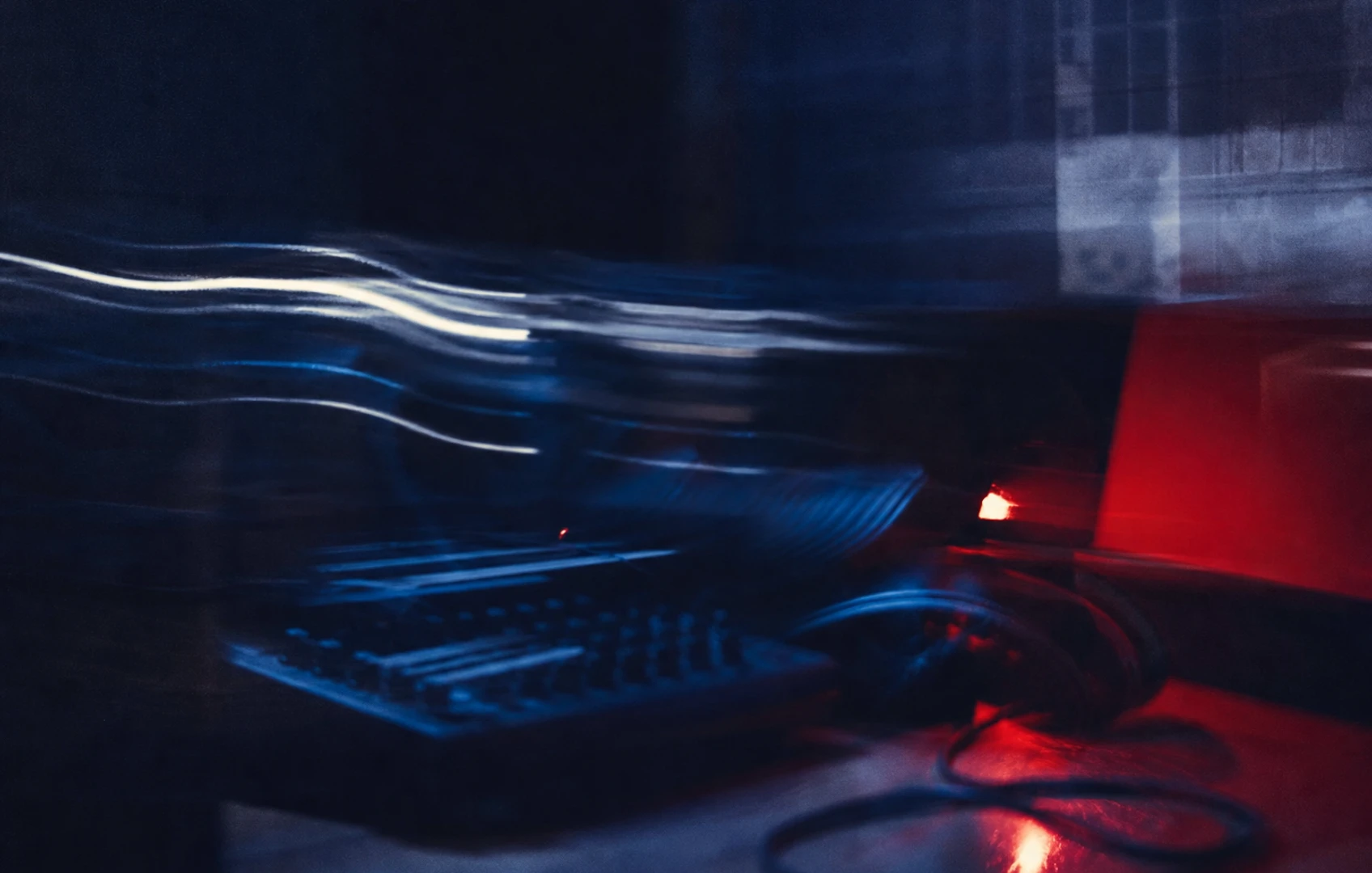 A moody cut-paper editorial image of a dim studio desk, sliced waveform shapes, sticky notes, and floating tape fragments in muted blues and warm red