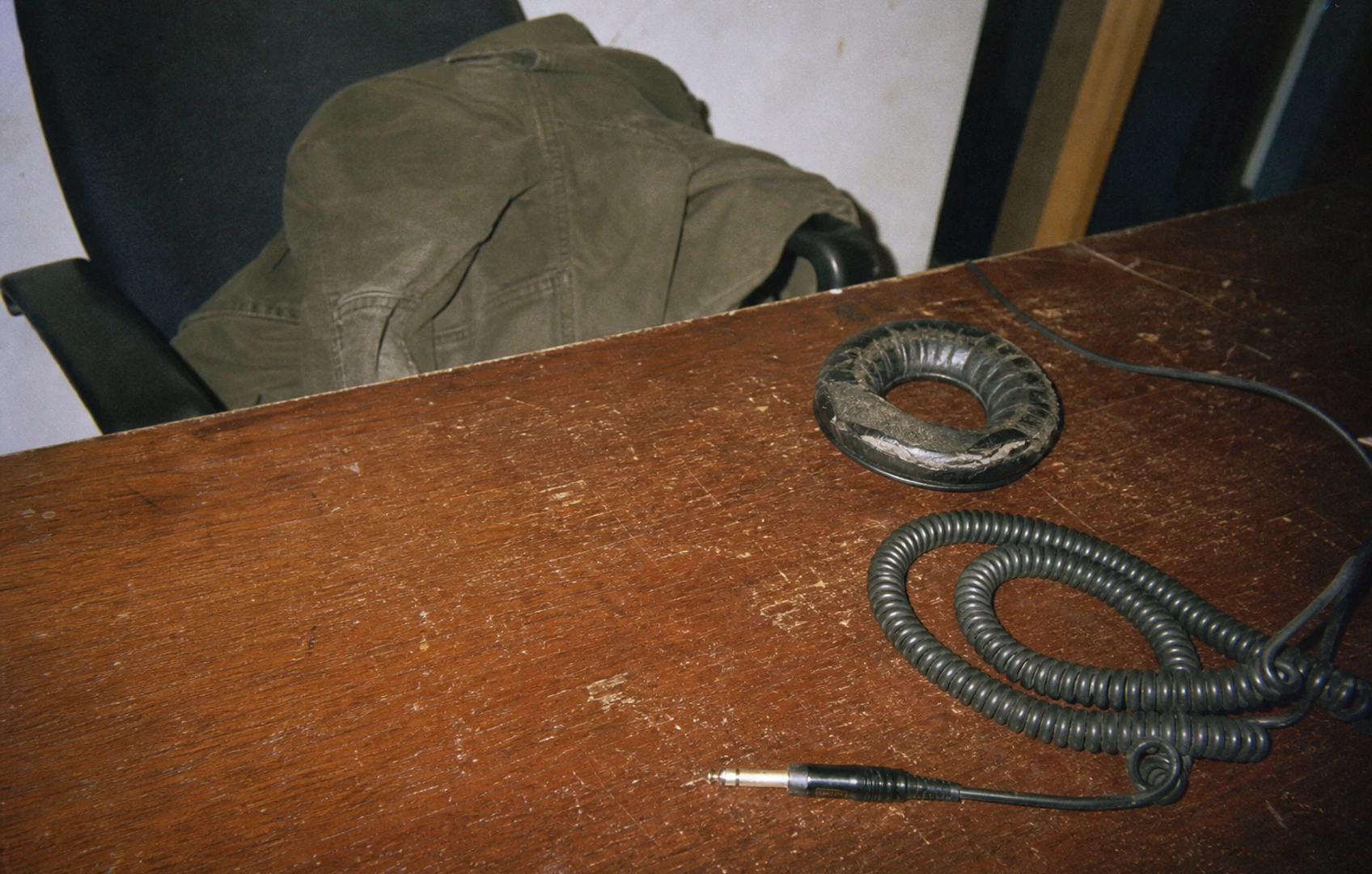 Scuffed color-photocopy artwork of a coiled audio cable and worn headphone cushion on a scratched desk, with a jacket slung over the chair behind it.